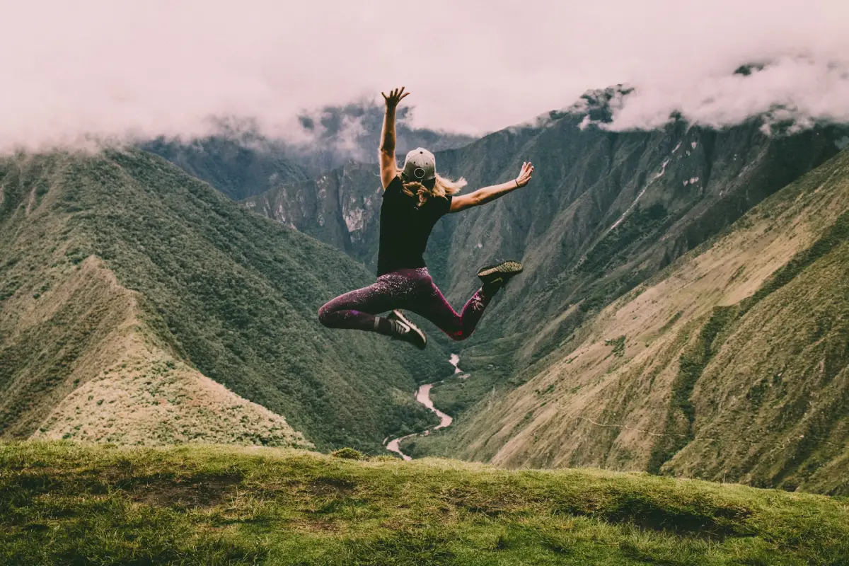 kvinna hoppar och poserar framför kamera vid ett berg